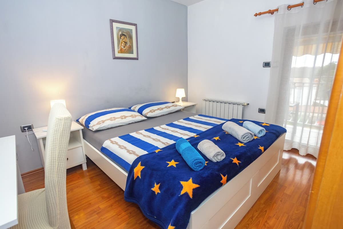 A double bed with a blue blanket featuring star patterns, two pillows, a bedside lamp, and a radiator.