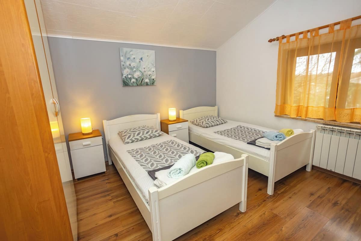 A room with two beds, a nightstand, a lamp, a painting, and a window with curtains.