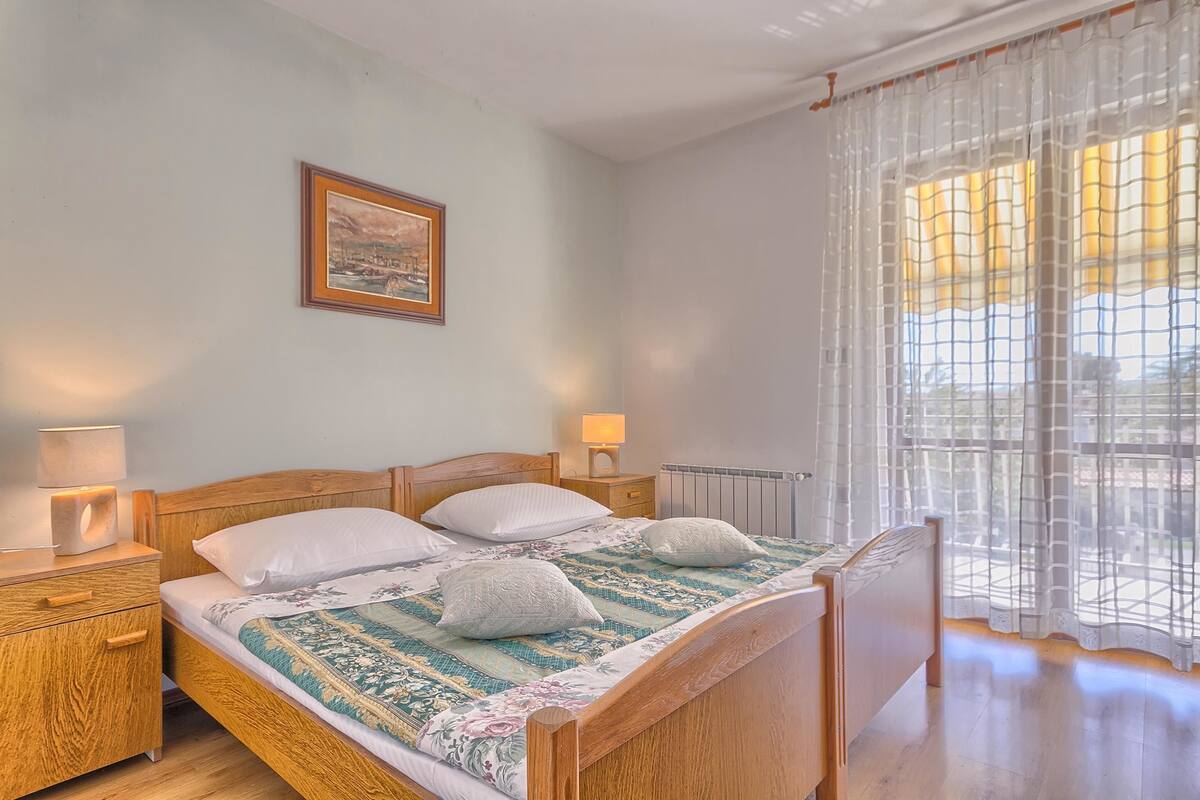 A neatly made bed with a floral bedspread, a bedside lamp, and a framed picture on the wall.