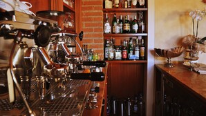 A bar area with a coffee machine, shelves of liquor bottles, and a decorative orchid arrangement. - Hotel La Corte (Bedizzole)