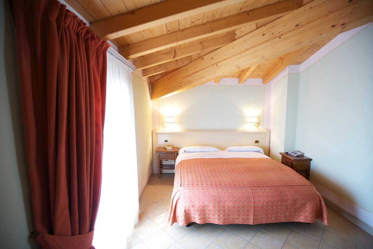 Un dormitorio con techo de madera, una cama con colcha estampada, lámparas de noche y una mesita.