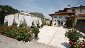 A courtyard with a white tent, red flowers, and a building with a tiled roof. - Hotel La Corte (Bedizzole)