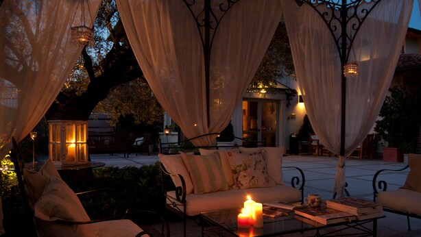 An outdoor seating area with a sofa, chairs, and a table with candles and books. - Hotel La Corte (Bedizzole)