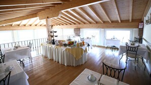 A spacious dining area with high wooden ceilings and large windows. Tables are set for dining, and a buffet table is centrally located with various food items. - Hotel La Corte (Bedizzole)