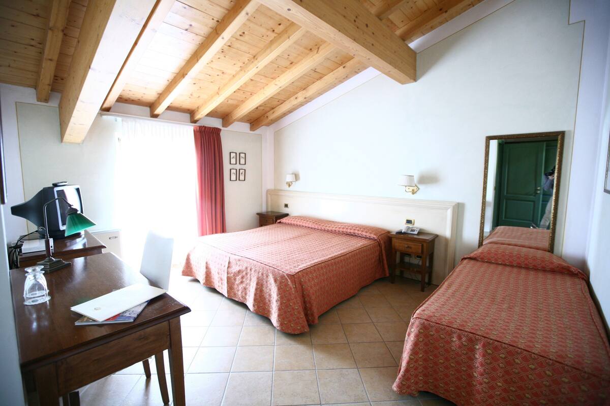 Una habitación con techo de madera, dos camas con ropa de cama coordinada, un escritorio con lámpara, una silla y un espejo en la pared.