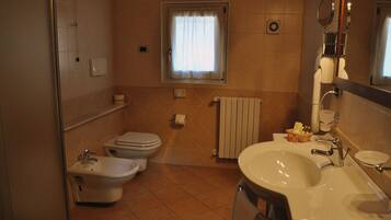 Ein Badezimmer mit Bidet, Toilette, Waschbecken und einem Fenster mit Vorhang.