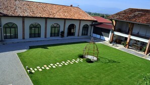 A spacious courtyard with a well-maintained lawn, a swing set, and a building with a tiled roof and arched windows. - Hotel La Corte (Bedizzole)