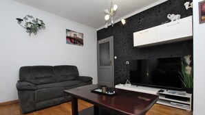 A living room with a dark brown sofa, a wooden coffee table, a flat-screen TV, and a white cabinet above the TV. - Apartment Ilinovic (Rovinj)