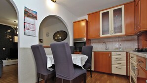 A compact kitchen with wooden cabinets, a dining table with chairs, and a wall-mounted calendar. - Apartment Ilinovic (Rovinj)