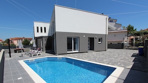 Uma casa moderna com piscina, um alpendre coberto e uma escadaria que dá para uma varanda.