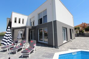 A modern two-story house with a swimming pool, outdoor seating, and a covered patio area.