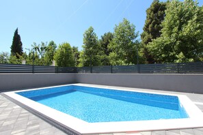 A rectangular swimming pool with a tiled edge, surrounded by a low wall and a metal fence.