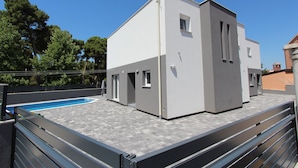 Um edifício moderno com telhado plano, piscina e cerca de metal.