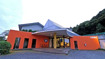 A modern building with a distinctive orange facade, a large entrance with a covered porch, and a sign in Japanese.
