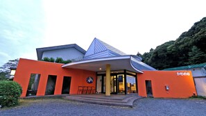 Un edificio moderno con una fachada naranja distintiva, una entrada amplia con porche cubierto y un letrero en japonés.