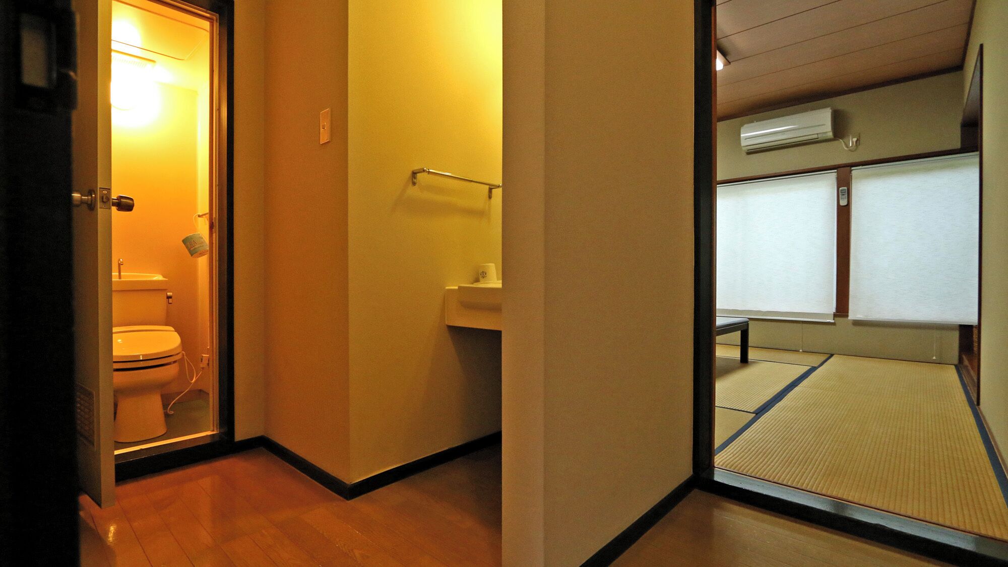 Un pasillo estrecho con un inodoro a la izquierda, un lavabo a la derecha y suelo de esteras de tatami.