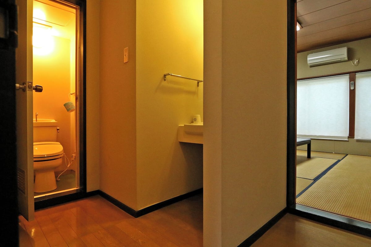 A narrow hallway with a toilet on the left, a sink on the right, and a tatami mat floor.