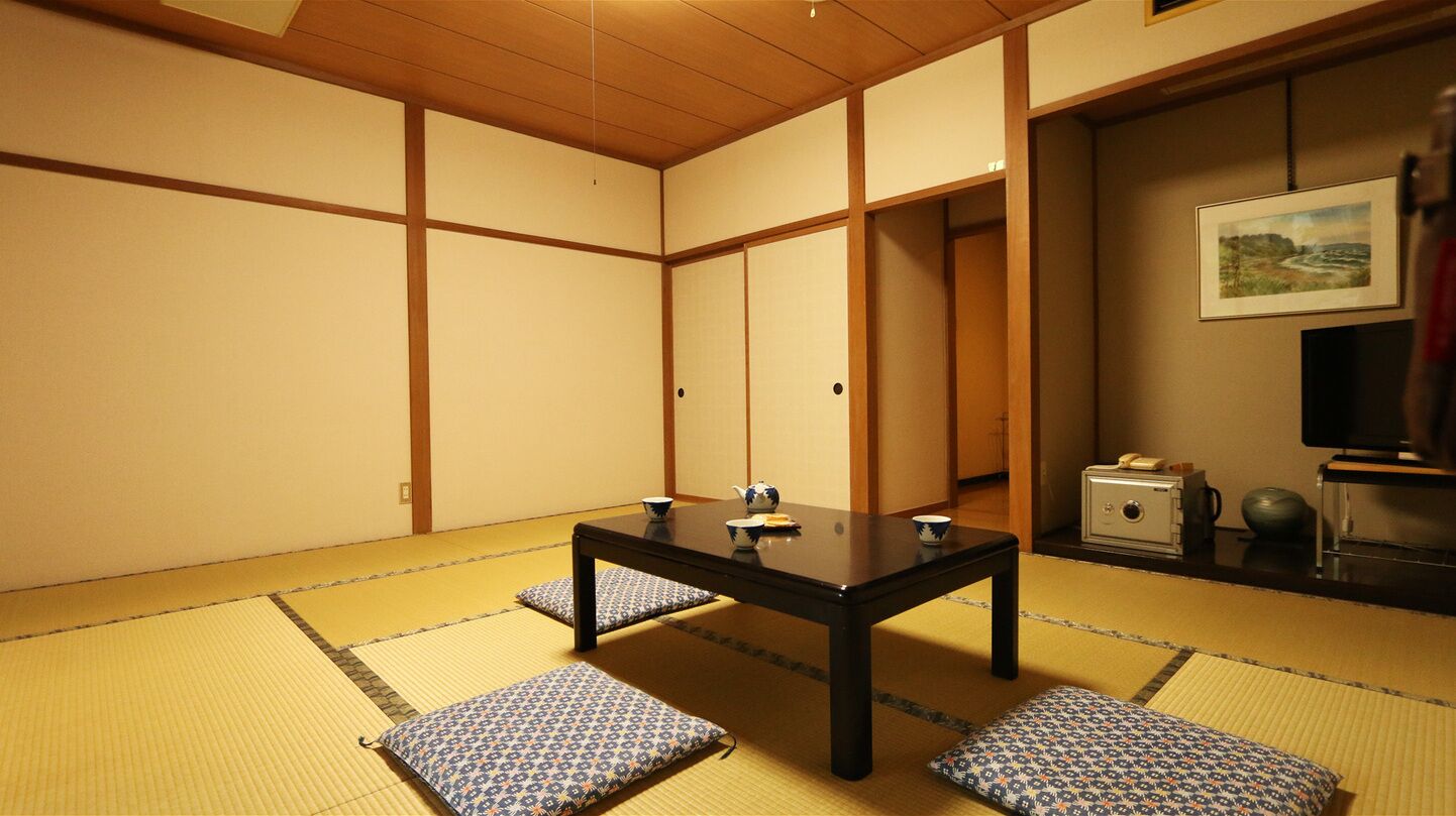Una habitación con esteras de tatami, una mesa baja, cojines, un televisor y una caja fuerte.