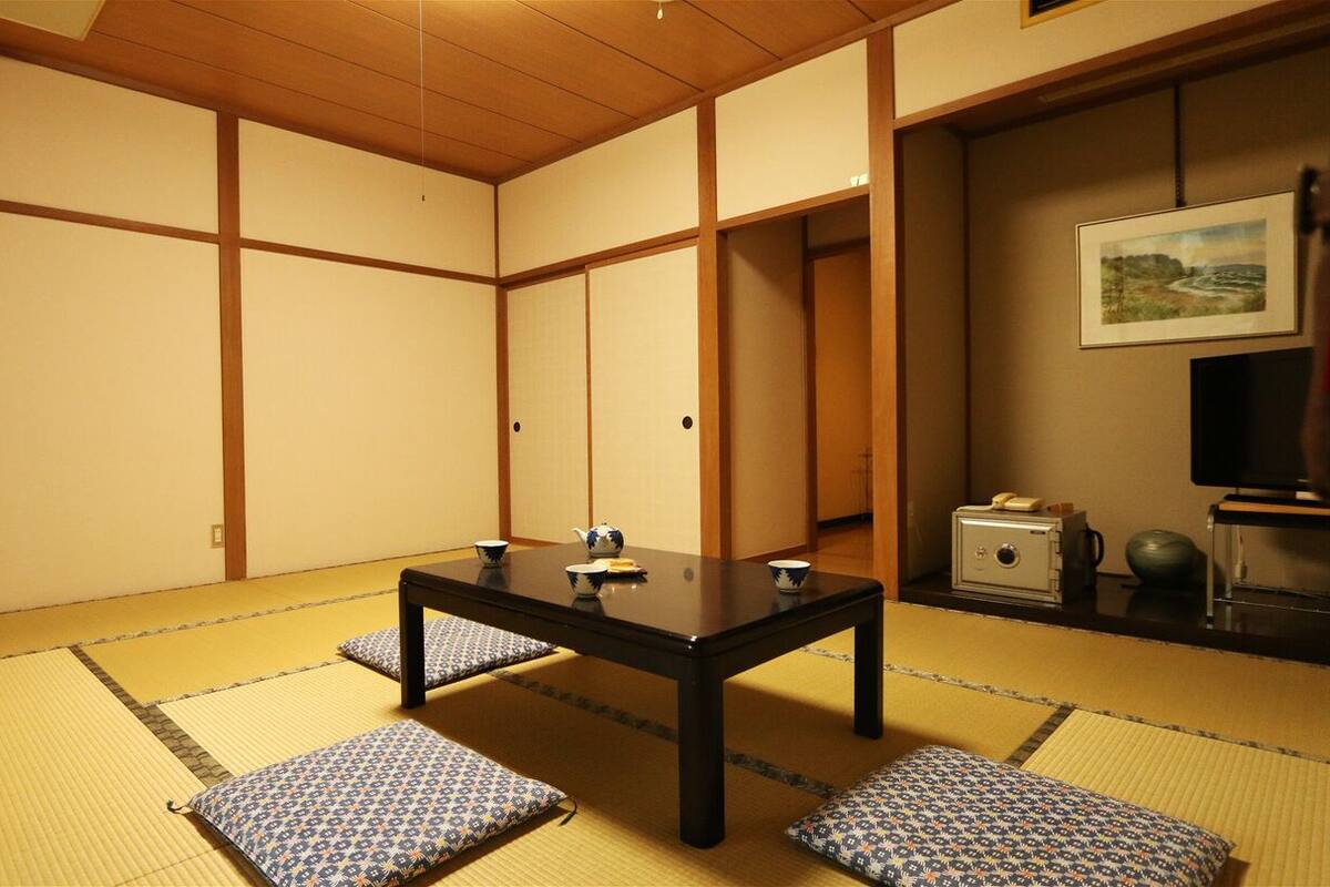 A tatami mat room with a low table, cushions, a television, and a safe.