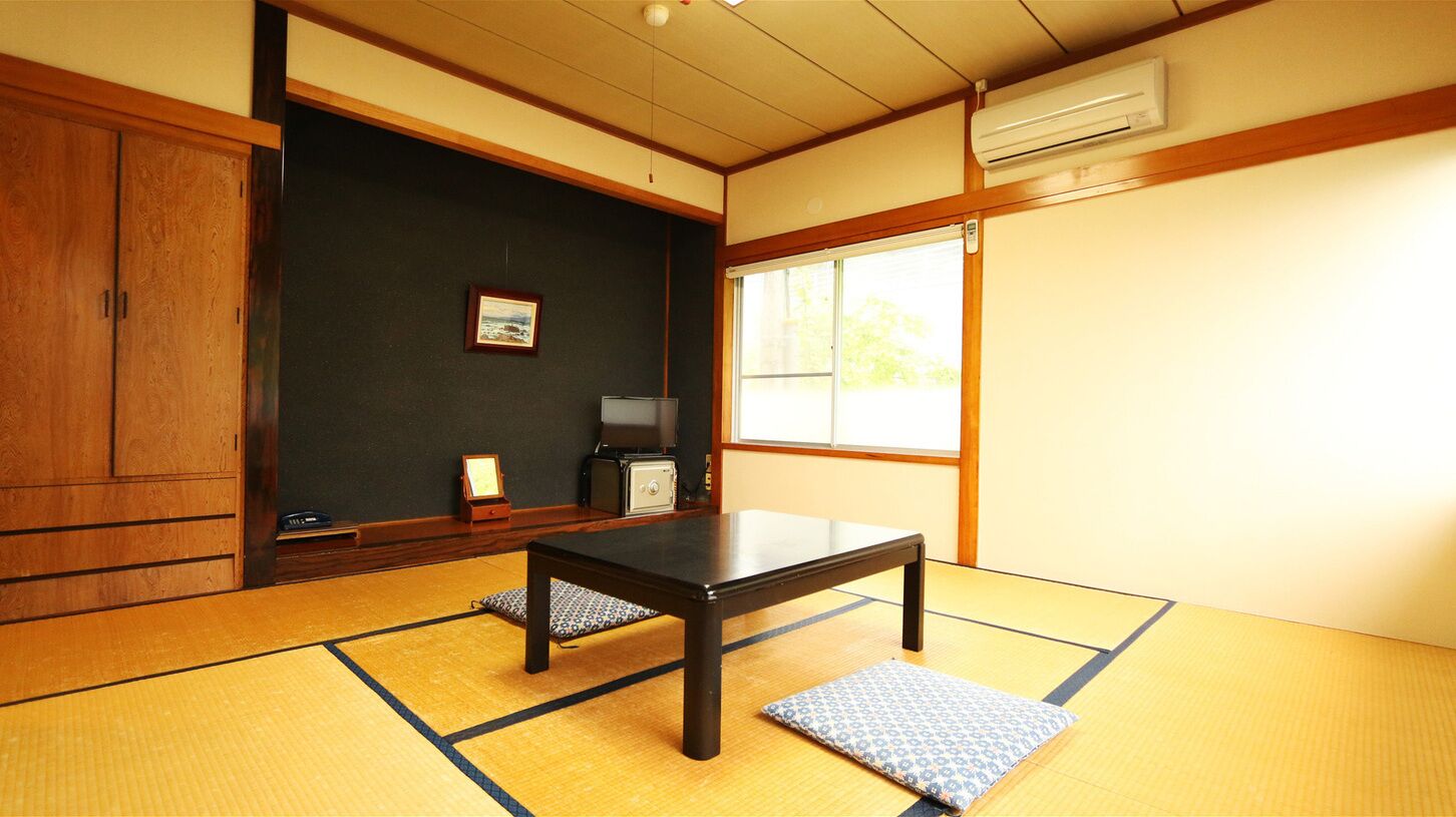 Una habitación con tatamis, una mesa baja, un televisor y una ventana.
