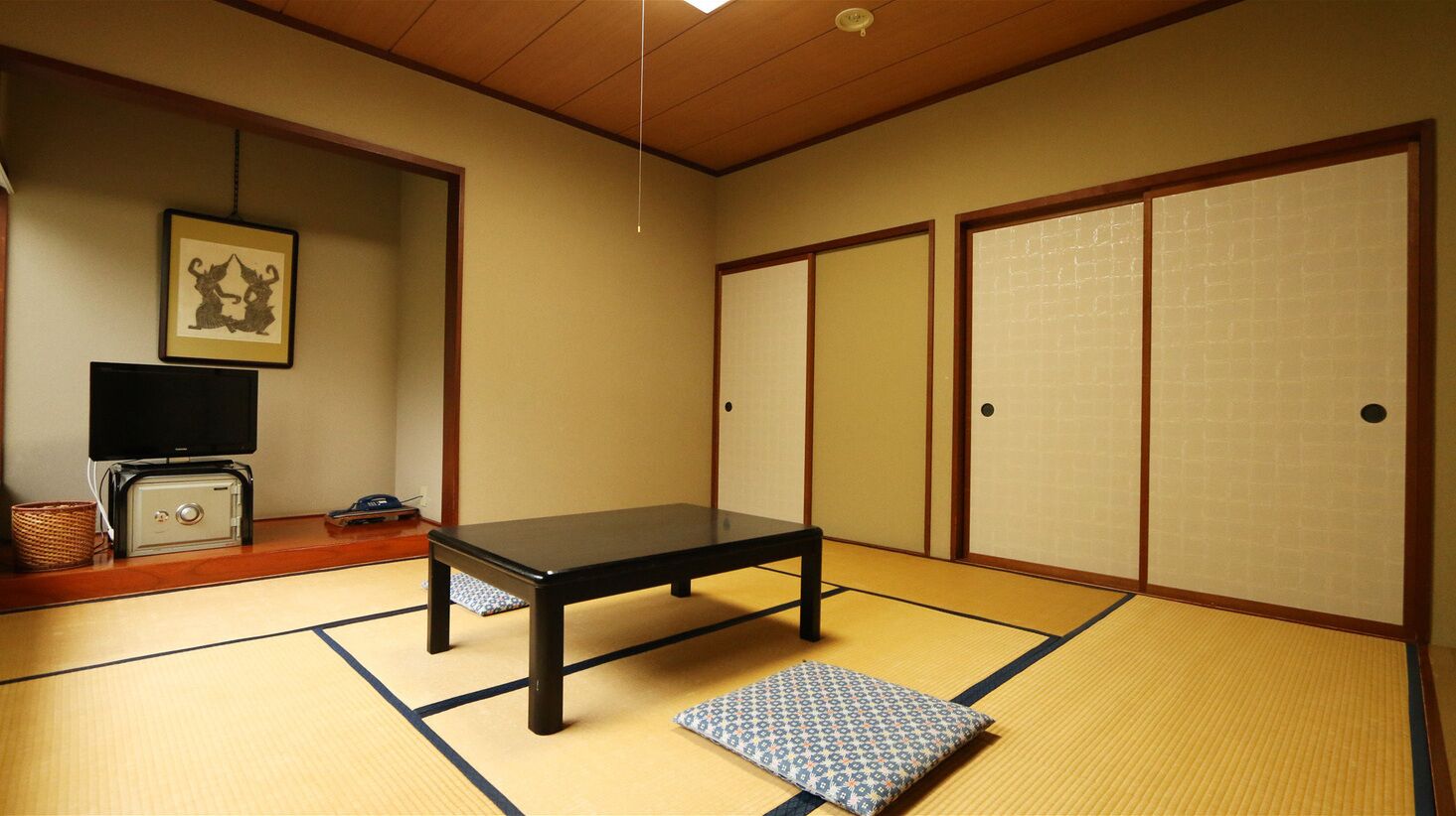 Una habitación japonesa tradicional con suelo de tatami, una mesa baja, puertas correderas y un televisor sobre un mueble.