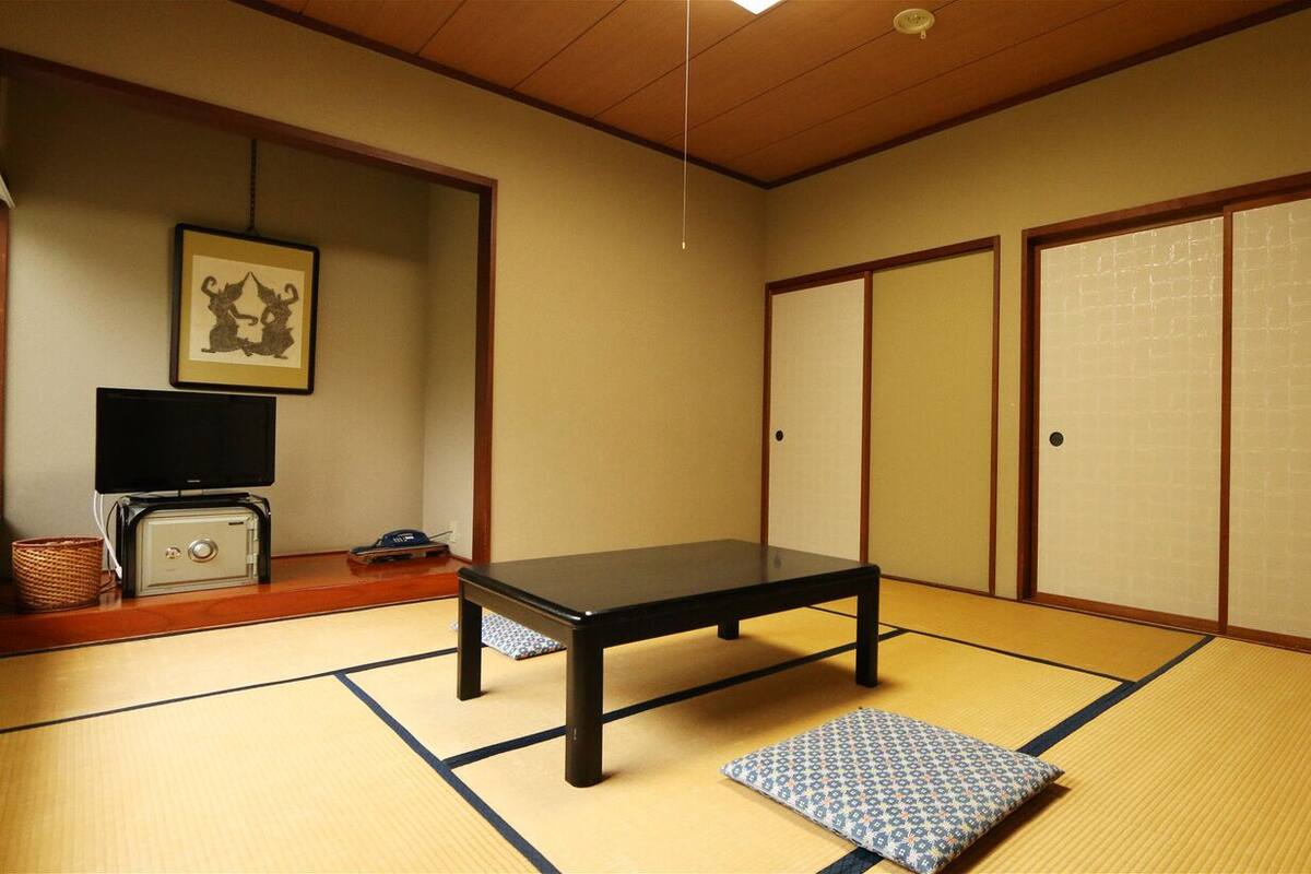 A traditional Japanese room with tatami flooring, a low table, sliding doors, and a television on a cabinet.