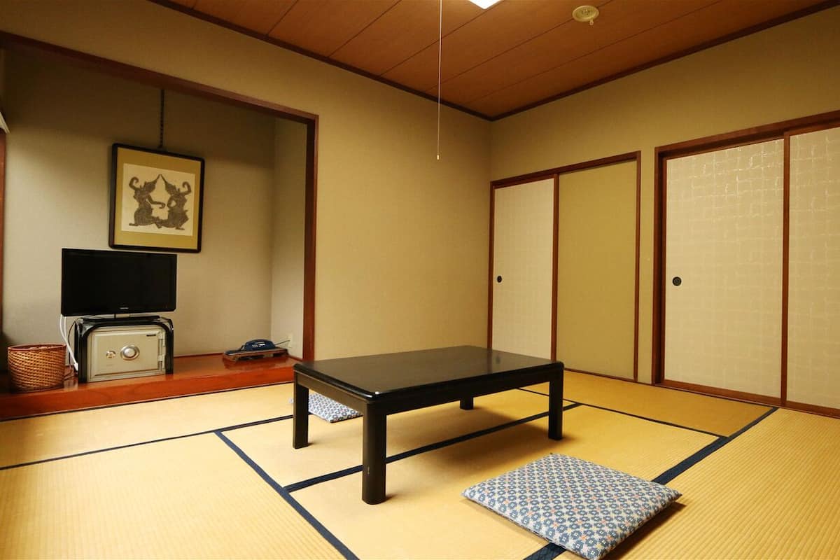 A traditional Japanese room with tatami flooring, a low table, sliding doors, and a television on a cabinet.