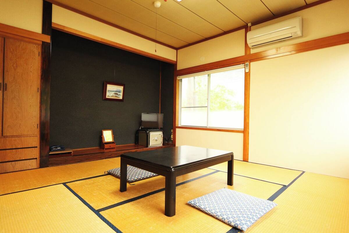 A traditional Japanese room with tatami flooring, a low table, a television, and a sliding door.