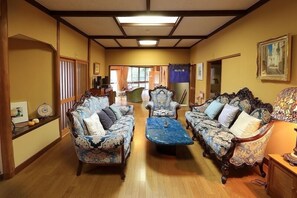 Una habitación tradicional japonesa con suelo de tatami, techo bajo y puertas correderas que dan a otra habitación.