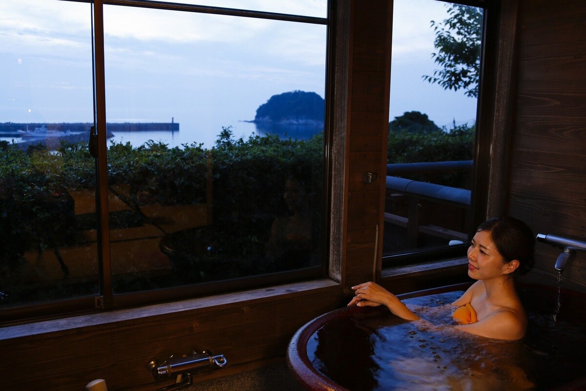 Eine Person in einer Hot Tub mit Blick auf ein Gewässer und Grünlandschaft.