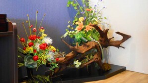 Two artificial floral arrangements on a black stand against a blue wall. - Business Hotel Isesaki Heisei INN (Isesaki)