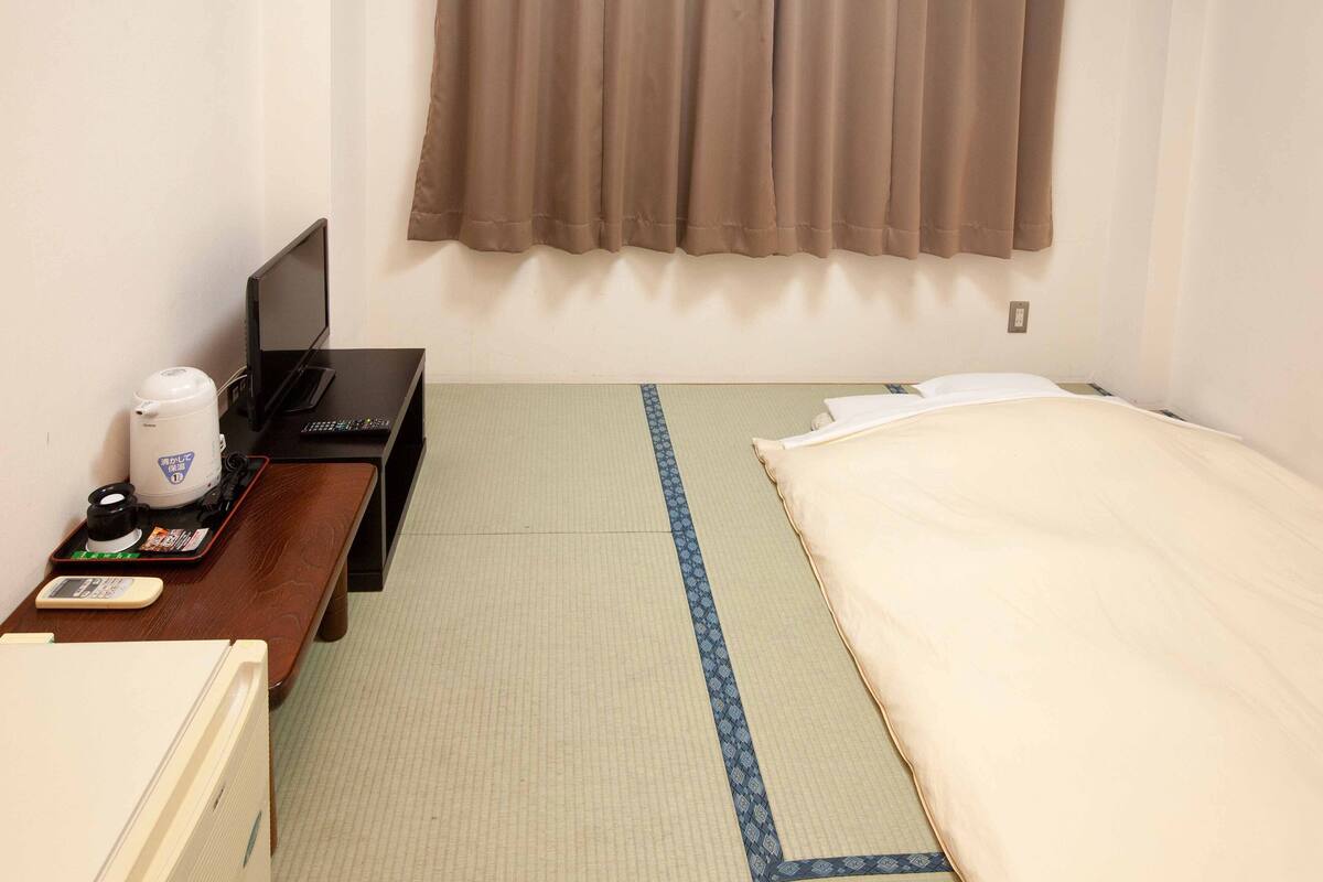 Une chambre d’hôtel comprenant un lit, un bureau avec une machine à café, une télévision et un sol recouvert de tatamis, ces nattes traditionnelles japonaises.