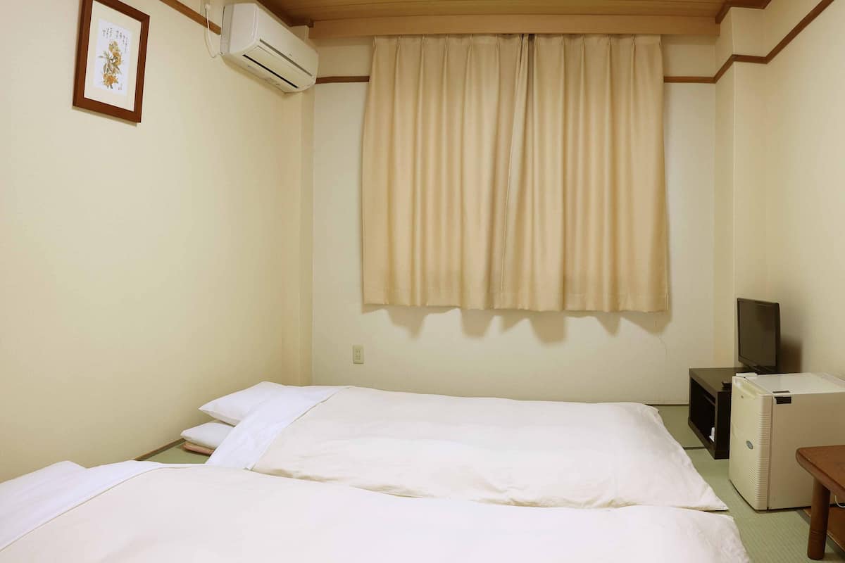 Une chambre d’hôtel avec deux lits, un appareil de climatisation, une télévision et une petite table.