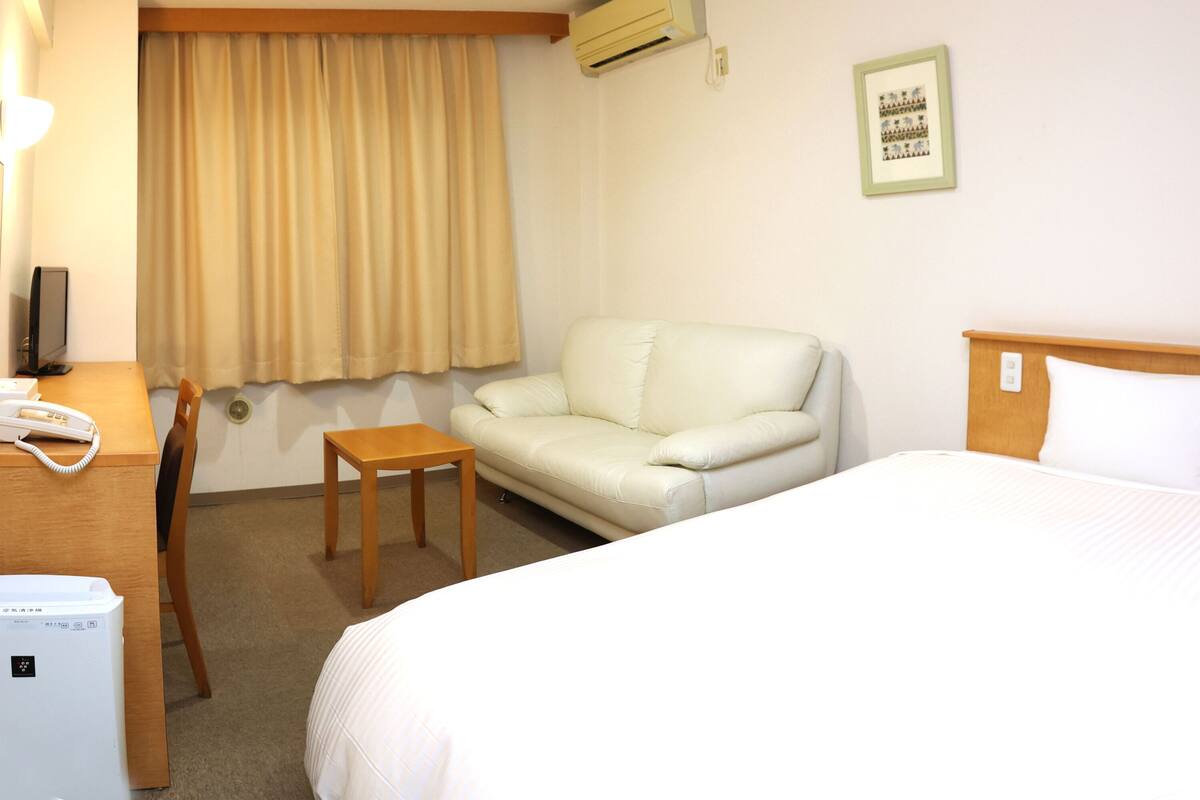 Une chambre d’hôtel comprenant un lit, une petite table, un canapé, un bureau avec un téléphone et un climatiseur fixé au mur.