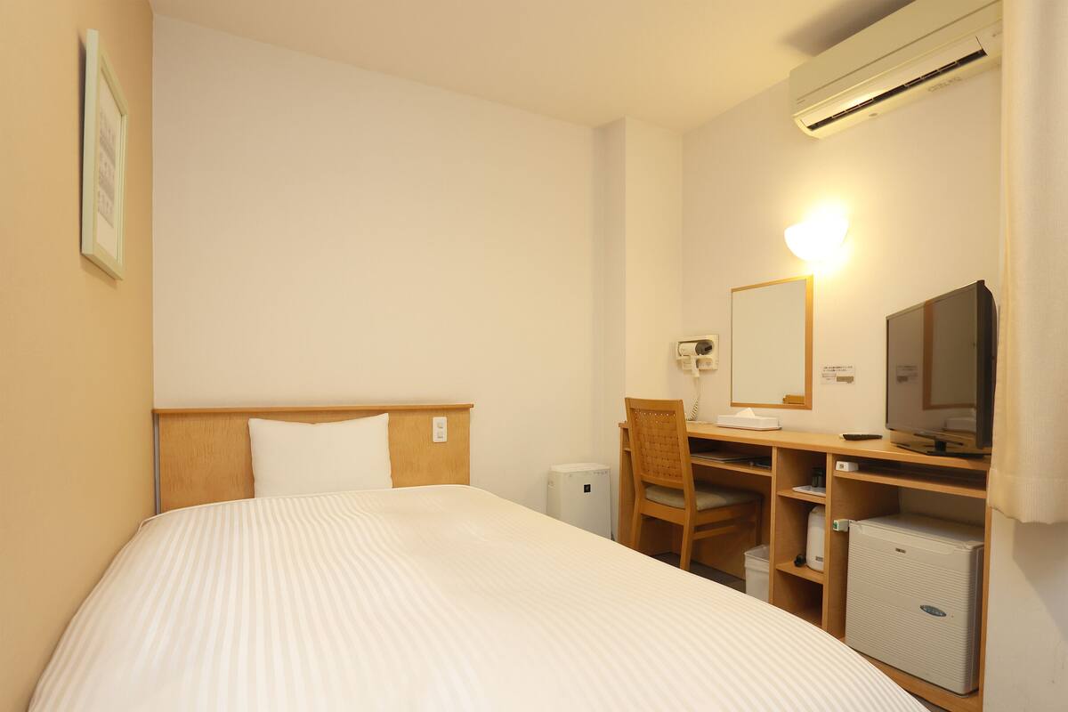 Une chambre d’hôtel comprenant un lit, un bureau avec une chaise, une télévision, un climatiseur et un miroir.