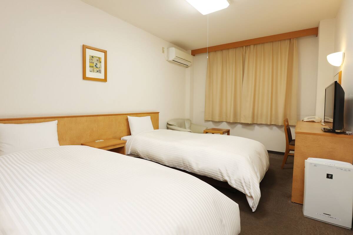 Une chambre d’hôtel avec deux lits, un bureau, une chaise, une télévision et un appareil de climatisation.