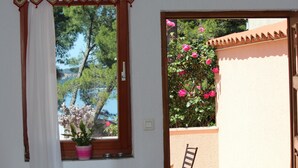 A window with a curtain, a potted plant, and a view of trees and a building. - Apartments Villa Lucu (Rovinj)