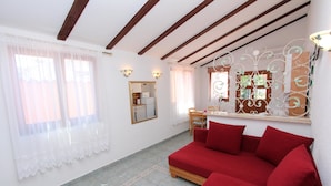 A room with a red sofa, a wooden-framed ceiling, a kitchen area, and a decorative mirror. - Apartments Villa Lucu (Rovinj)
