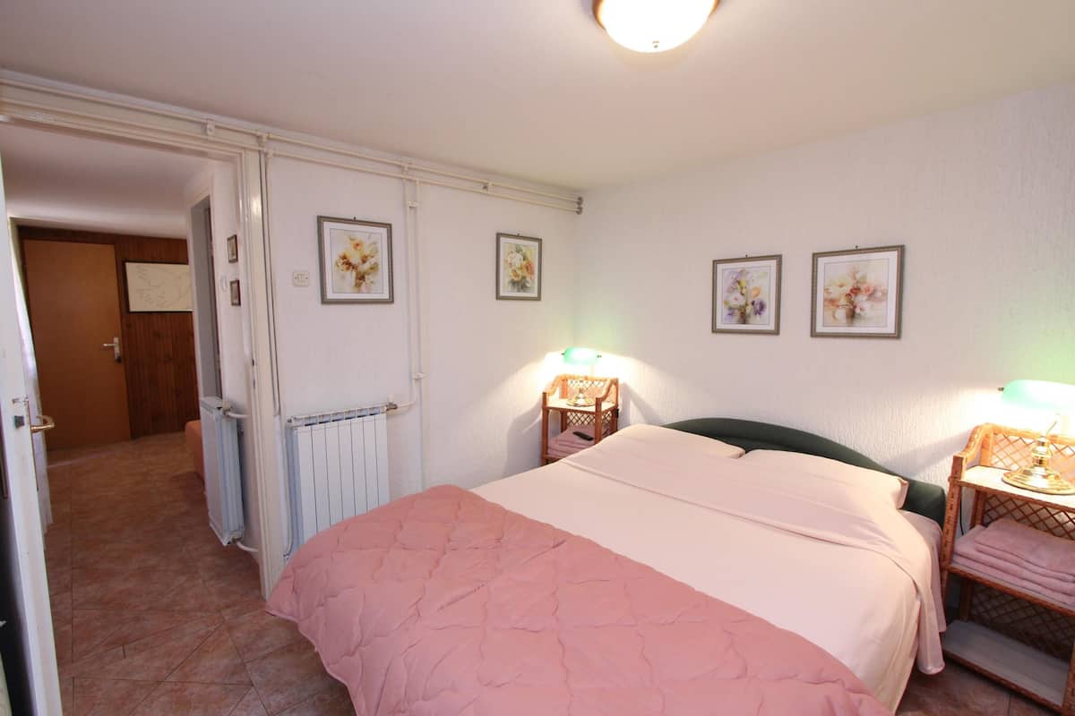 A bedroom with a bed, two bedside tables with lamps, a radiator, and framed floral artwork on the wall.