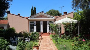 A two-story building with a central entrance, a covered patio area, and a garden with potted plants and outdoor furniture. - Apartments Villa Lucu (Rovinj)