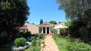 A garden pathway leading to a building with a central entrance, surrounded by lush greenery and flowering plants. - Apartments Villa Lucu (Rovinj)
