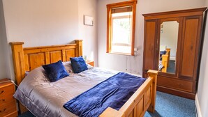 Ein Schlafzimmer mit einem hölzernen Bett, einem Nachttisch, einer Kommode und einem Fenster mit Blick ins Freie.