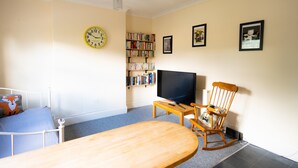 Ein Wohnzimmer mit einem Bett, einem Fernseher, einem Bücherregal und einer Uhr an der Wand.