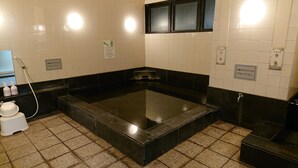 A bathroom with a large black bathtub, white tiled walls, and a small white stool. - Hotel Castle Plaza Tagajo (Tagajo)