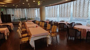 A restaurant with multiple tables and chairs, large windows with curtains, and a view of buildings outside. - Hotel Castle Plaza Tagajo (Tagajo)