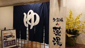 A room with a large wooden door, a dark blue curtain with a white design, a framed sign with Japanese text, and a potted yellow orchid plant. - Hotel Castle Plaza Tagajo (Tagajo)