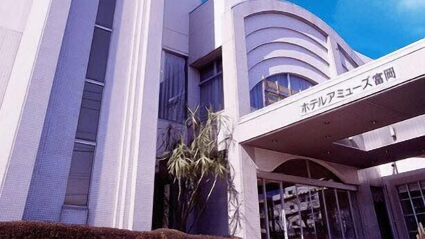 A modern building with a curved facade and a sign indicating it is a hotel. - Hotel Amuse Tomioka (Tomioka)