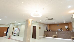 Zona de recepción de un hotel con mostrador, dos sillas de madera, un reloj en la pared y una máquina expendedora.