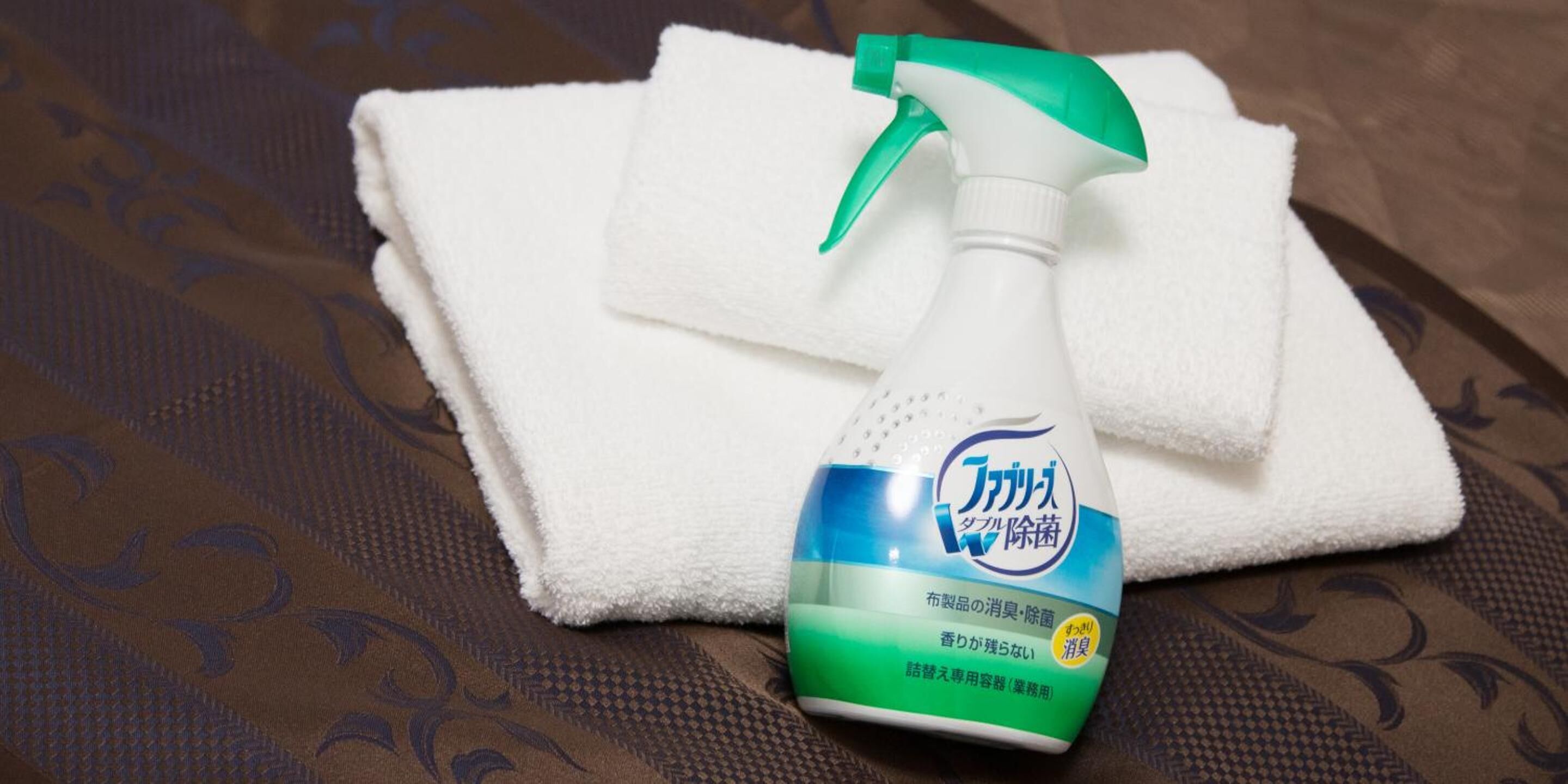 A spray bottle with a label on a folded white towel on a patterned fabric surface.