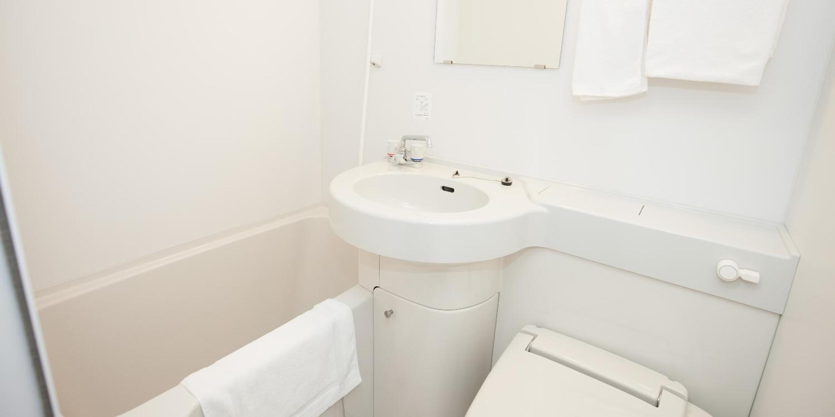 Ein kleines, weißes Badezimmer mit Waschbecken, Spiegel und Toilette.